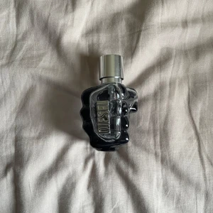 Diesel Only The Brave Parfym - Cool parfym från Diesel i en unik flaska formad som en knytnäve. Flaskan är genomskinlig med mörkblå och silverdetaljer samt ett silverfärgat lock. Passar dig som gillar statement-dofter och snygg design på hyllan.