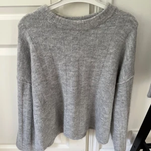Ljusgrå stickad tröja från Gina Tricot - Mysig ljusgrå stickad tröja från Gina Tricot. Tröjan har en rund halsringning och långa ärmar. Perfekt för kyligare dagar och enkel att matcha med olika outfits.