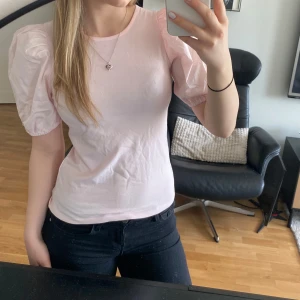 Ljusrosa topp med puffärmar - Säljer en ljusrosa topp med korta puffärmar och rund halsringning. Toppen har en feminin och söt stil, perfekt att matcha med jeans eller kjol. Materialet känns mjukt och bekvämt mot huden.