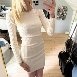 Beige ribbad långärmad klänning - Säljer en beige ribbad klänning med lång ärm och tight passform. Klänningen är kort och har en snygg omlottdetalj i ryggen som ger en unik look. Perfekt för dig som gillar stilrena och enkla plagg med en twist.