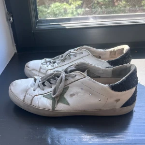 Vita sneakers från Golden Goose med grön stjärna - Säljer ett par vita sneakers från Golden Goose med grön stjärndetalj på sidan och svart glittrig häl. Inte så bra skick och slitna, men går absolut fortfarande att använda och passar ändå in till golden goose ’redan använda’ stil. Pris kan därför diskuteras. 