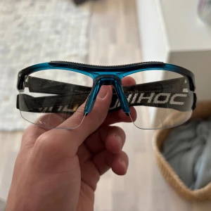 Blå innebandys glasögon från Unihoc - Säljer ett par blåa innebandys glasögon från Unihoc med justerbart svart band och genomskinliga linser. Skriv för fler frågor eller bilder i chatten tack!