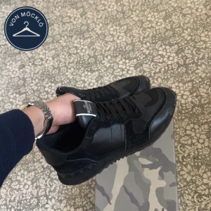 Svarta Valentino Rockrunner sneakers - Säljer ett par svarta Valentino Rockrunner sneakers med kamouflagemönster och svarta detaljer. Skorna har snörning, rund tå och platt sula.🤩Klassisk logga på plösen och cool design som sticker ut. Man ser att skorna har använt, så det är därför dem inte är i topp skick.(finns även två lagade hål på vänster och höger skon) Pris kan diskuteras vid snabb affär✅Inget kvitto❌