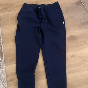 Mörkblå mjukisbyxor från Polo Ralph Lauren - Mörkblå mjukisbyxor från Polo Ralph Lauren med dragsko i midjan och broderad logga på ena benet. Byxorna har en avslappnad passform och är perfekta för en chill stil.
