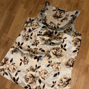 Blommig linnetopp med leoparddetaljer - Säljer en snygg linnetopp med stora blommor i beige och brunt på ljus bakgrund. Kragen har leopardmönstrad kant som ger en cool kontrast. Perfekt för dig som gillar unika detaljer och mönster!