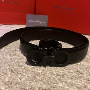 Svart skärp från Salvatore Ferragamo - Säljer ett svart skärp från Salvatore Ferragamo med en ikonisk dubbel-Gancini-spänne i svart metall. Skärpet är gjort i präglat skinn och har en stilren, modern design. Perfekt accessoar för att lyfta din outfit.
