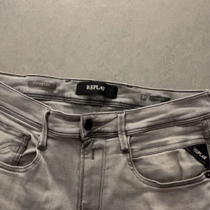 Replay Hyperflex Anbass grå jeans - Säljer ett par grå Replay Hyperflex Anbass jeans med klassisk femficksdesign och snygga detaljer på bakfickorna. Jeansen är stretchiga och har en slim passform som sitter riktigt snyggt. Perfekta för dig som gillar stilrena och bekväma jeans.