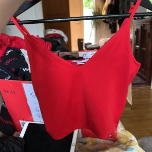 Röd linnetopp från Amisu - Snygg röd linnetopp från Amisu med smala, justerbara axelband och v-ringad hals. Toppen är i mjuk och stretchig polyester, perfekt för att lyfta vilken outfit som helst. Enkel och stilren design som är lätt att matcha med jeans eller kjol.