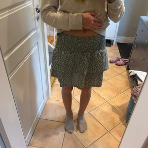 Grön blommig volangkjol - Supersöt grön kortkjol med vita småblommor och bred smock i midjan. 