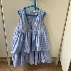 Blåvit randig volangklänning - Supersöt blå och vit randig klänning med volanger och v-ringning. Med inbyggda shorts. Perfekt för varma dagar.