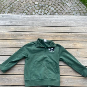 Grön Nike half zip sweatshirt - Grön sweatshirt från Nike med broderad N-logga och swoosh på bröstet. Tröjan har half zip, hög krage och en stor magficka. Tillverkad i mjuk bomull och har långa ärmar. Perfekt för en chill och sportig look.
