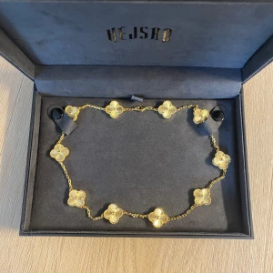Kejsar halsband  - Stilrent halsband i guld med flera fyrklöverformade blommor längs kedjan. Blommorna har räfflade detaljer och en liten guldkula i mitten, vilket ger ett lyxigt och unikt intryck. Perfekt accessoar för att lyfta vilken outfit som helst.