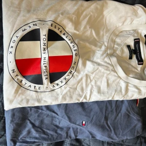 2-pack Tommy Hilfiger t-shirts XS - Två snygga t-shirts från Tommy Hilfiger i storlek XS. En vit med stort tryck och logga framtill i svart, rött och blått, och en marinblå med liten broderad logga på bröstet. Båda är i mjuk bomull och har klassisk rund hals och kort ärm.