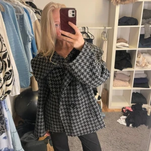 Oversized rutig jacka  - Säljer en oversized jacka med stort rutigt mönster i svart och grått. Jackan har bred krage, stora knappar framtill och långa ärmar. Perfekt för dig som gillar statement-plagg och vill ha en unik look.