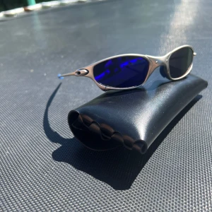 Oakley solglasögon blå lins - Snygga Oakley solglasögon med futuristisk silverfärgad metallbåge och spegelblå ovala linser. Unik design med coola detaljer vid gångjärnen. Perfekta för dig som vill sticka ut och gillar sportig stil. Kommer med svart hårt fodral.