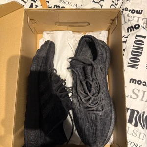 Svarta Adidas Ultraboost sneakers - Svarta Adidas Ultraboost sneakers med stickad ovandel och klassisk Boost-sula. Skorna har rund tå, snörning och en stilren, helsvart look som passar perfekt till streetwear. Superbekväma och lätta, perfekta för dig som gillar både stil och komfort.