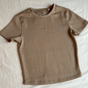 Beige ribbad t-shirt från Nicce - Säljer en beige ribbad t-shirt från Nicce i storlek xs. Den har använts en gång och nu är den för liten. Säljer T-shirten för 50kr men du kan få hela sättet för 120kr🤍
