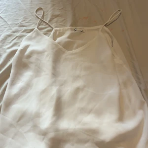 Vit linnetopp från C strl 34 - Säljer en stilren vit linnetopp från C i storlek 34. Toppen har tunna axelband och v-ringning, perfekt för varma dagar eller att styla lager på lager. Materialet känns lätt och luftigt, vilket gör den superbekväm att bära.