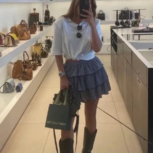 Rutig volangkjol från Zara - Supersöt kort volangkjol från Zara i svartvitt rutigt mönster. Kjolen har flera lager volanger och resår i midjan för en bekväm passform. Perfekt att styla med boots eller sneakers för en trendig look.