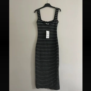 Svartvit randig långklänning från Zara - Svart långklänning med vita horisontella ränder och breda axelband. Klänningen har en tight passform och är ärmlös med fyrkantig ringning. Perfekt för dig som gillar en enkel men stilren look.