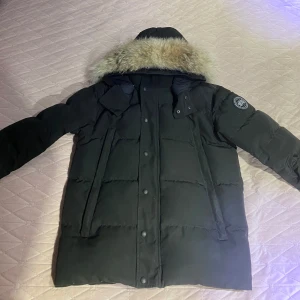 Canada Goose Wyndham Parka - Säljer en svart dunjacka av canada goose black label i mycket bra skick. Man kan ta bort och sätta på pälsen. Den har 6 fickor och varm för kalla vinter dagar. Den är i storlek S men kan passa M också. DEN ÄR ÄKTA!!!