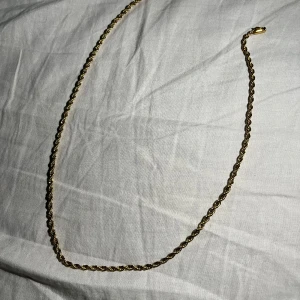Guldfärgat tvinnat halsband - Snyggt guldfärgat halsband med tvinnad kedja som ger en stilren och trendig look. Kedjan har en klassisk karbinhake och passar perfekt för att lyfta vilken outfit som helst. Perfekt för dig som gillar enkla men ändå iögonfallande smycken.