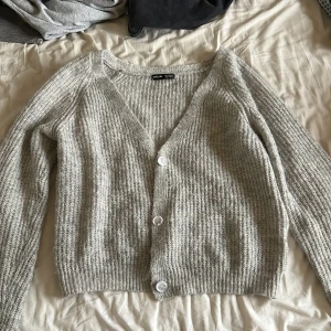 Grå ribbad kofta från SHEIN - Mysig grå kofta från SHEIN i storlek S. Den är stickad med ribbad struktur, har v-ringning och tre vita knappar framtill. Perfekt att slänga på sig över en t-shirt eller linne. Långärmad och croppad modell som ger en chill vibe.