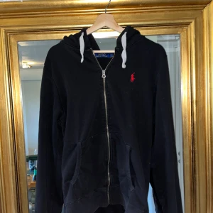 Svart Polo Ralph Lauren Hoodie - Säljer en svart hoodie från Polo Ralph Lauren med dragkedja! Den är i riktigt bra skick men är lite för stor. Riktigt go tröja att ha för lite kyligare dagar pga sitt mjuka och varma innetyg. Hör av er vid funderingar!🙏