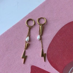 Guldiga örhängen med blixt och pärla - Snygga guldiga örhängen med ring och hängande kedjor, dekorerade med en vit droppformad pärla, konformad detalj och cool blixt. Ger en edgy vibe och sticker verkligen ut. Perfekt accessoar för dig som vill ha något unikt och trendigt.
