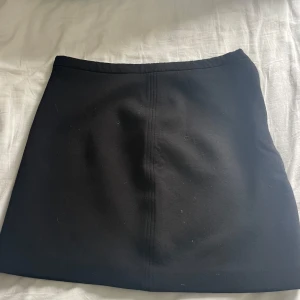 Svart kortkjol från & Other Stories - En svart, stilren kortkjol från & Other Stories med rak passform och synlig guldfärgad dragkedja i sidan. 