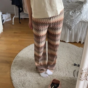 Mönstrade wide byxor i pastell - Säljer ett par snygga byxor med zigzag-mönster i beige, rosa och bruna toner. Byxorna har en loose och wide passform med raka ben och elastisk midja. Perfekta för dig som gillar färg och mönster i din outfit. OBS byxorna är lite slitna ner till men ej hål i dem. Några trådar har gått upp. 