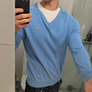 Ljusblå v-ringad tröja Morris L - Snygg ljusblå v-ringad tröja från Morris med broderad orange logga på bröstet. Tröjan är i mjuk bomull och har ribbade muddar vid ärmslut och nederkant. Perfekt för dig som gillar stilren och klassisk look.