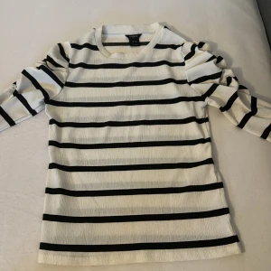 Randig långärmad tröja från Lindex - Säljer en vit och svart randig långärmad tröja från Lindex i storlek XS. Tröjan har puffade axlar och är tillverkad i ett strukturerat, stretchigt material. Perfekt för dig som gillar en klassisk men trendig look.
