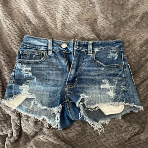 Blå jeansshorts från American Eagle - Snygga blå jeansshorts från American Eagle med slitna detaljer och fransig kant. Modellen är högmidjad och har klassiska fickor både fram och bak. Superstretch-material för extra bekvämlighet. Perfekta för varma dagar och en avslappnad look. Lågmidjade i st xs❤️