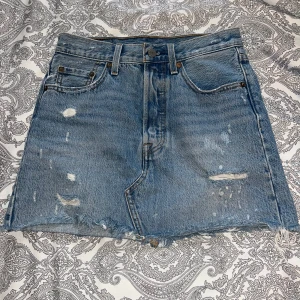 Vintage Levi's jeanskjol med slitna detaljer - Superfin vintage jeanskjol från Levi’s i blå tvätt med slitningar och fransad kant. Köpt för många år sen men aldrig använd av mig – tyvärr är den för liten nu :(  Kjolen har Levi’s klassiska detaljer som läderpatch, röd tagg och märkta knappar, men saknar modellnummer på inneretiketten (vanligt på äldre och vintage plagg). Men är äkta! Storleken är 24, vilket motsvarar storlek XS! Ordinarie pris var 1500kr