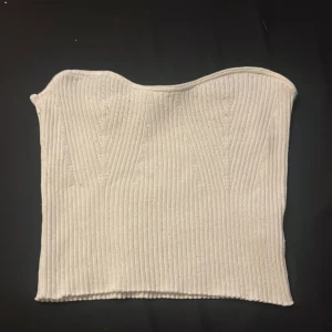 Vit ribbad tubtopp från H&M Divided - Säljer en vit ribbad tubtopp från H&M Divided i storlek M. Toppen är bandeau-modell och har en snygg, vågig kant upptill. Perfekt att styla med jeans eller kjol för en clean look.