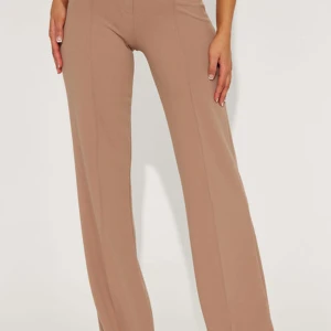 Beiga vida kostymbyxor med hög midja - Snygga beiga kostymbyxor med hög midja och vida ben. Byxorna har en unik knäppning framtill och markerad söm längs benen för en clean look. Perfekta att styla med crop top eller skjorta för en trendig vibe.