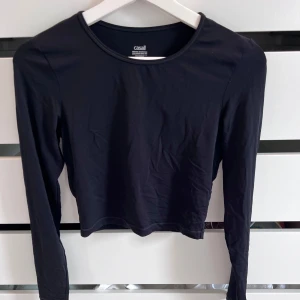 Svart långärmad topp från Casall - Snygg svart långärmad topp från Casall med rund halsringning och croppad passform. Perfekt för träning eller chill dagar. Tillverkad i mjukt och stretchigt syntetmaterial som sitter skönt på kroppen.