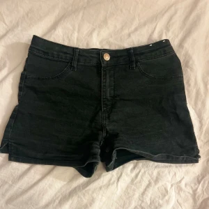 Svarta jeansshorts med hög midja - Snygga svarta jeansshorts med hög midja och klassisk femficksdesign. De har bälteshällor, knapp och dragkedja framtill samt uppvikta benslut. Perfekta för sommardagar och enkla att matcha med allt.