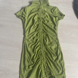 Grön ribbad kortklänning från SHEIN - Snygg grön ribbad kortklänning från SHEIN med kort ärm, hög krage och knappar längs hela framsidan. Klänningen har rynkade detaljer framtill som ger en cool och trendig look. Perfekt för dig som gillar att sticka ut med färg och form.