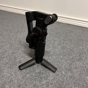 3-axis smartphonestabilisator -  Säljer min 3-axis smartphonestabilisator – perfekt för dig som vill ta dina mobilvideos till nästa nivå! Den är i toppskick och fungerar felfritt.   Funktioner: 	•	AI-spårning: Följer automatiskt ansikten och kroppsrörelser ,perfekt för vloggar, träning eller livesändningar. 	•	Proffsig stabilisering: Filma smidigt och skakfritt oavsett om du går, springer eller rör dig snabbt. 	•	Flera filmfunktioner: Timelapse, slow motion, panoramabilder m.m.  allt enkelt tillgängligt i appen. (Alla mobiler)
