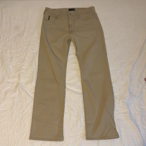 Beige byxor från Armani Jeans - Snygga beige byxor från Armani Jeans med klassisk femficksdesign. Byxorna har raka ben och normal passform. Tillverkade i bomull med lite stretch för extra komfort. Perfekta för en clean och stilren look.