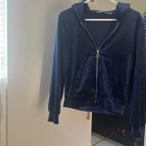 Mörkblå velour hoodie med dragkedja - Mysig mörkblå hoodie i mjuk velour med huva och silverfärgad dragkedja framtill. Jackan har långa ärmar och en stor ficka på magen. Perfekt för en chill och avslappnad stil.