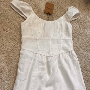 Vit kortklänning korsettliknande  - Superfin vit kortklänning från Sellpy med breda axelband och markerad midja- korsettlikande! Klänningen har en enkel, stilren design och är gjord i ett svalt linnematerial som passar perfekt till varma dagar! Lappen kvar från Sellpy 