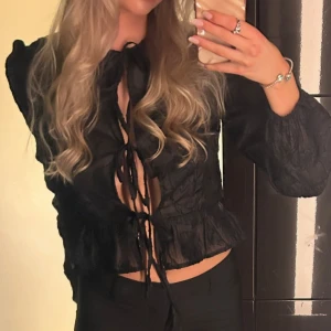 Svart blus med puffarmar  - Svart blus med puffarmar, volang i slutet och knytning i mitten. Snygg och skön blus. Strl 38 men är som en 36