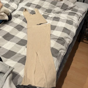 Beige ribbad långklänning Gina Tricot - Supersnygg beige ribbad långklänning från Gina Tricot. Klänningen är ärmlös med breda axelband och har en slits framtill för extra vibe. Stickad i mjukt material som sitter skönt och ger en clean look. Perfekt för dig som gillar stilrena och trendiga outfits.
