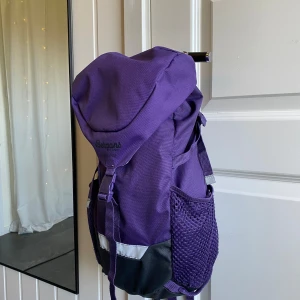 Lila ryggsäck från Bergans - Säljer en lila barnryggsäck från Bergans med smarta fack och meshficka på sidan. Väskan har justerbara remmar, spänne framtill och reflekterande detalj längst ner. Perfekt för dig som vill ha en snygg och praktisk väska till vardagen eller utflykten.