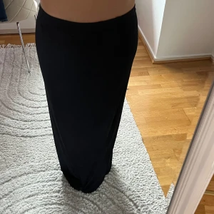 Svart långkjol i mjukt material - Enkel och stilren svart långkjol med rak passform och resår i midjan. Kjolen är figurnära upptill och faller snyggt längs benen. Perfekt för dig som gillar minimalistisk stil och vill ha en klassisk bas i garderoben.