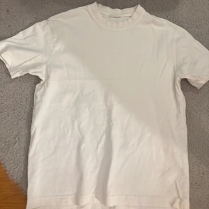 Vit basic t-shirt i bomull - Enkel och stilren vit t-shirt i mjuk bomull. Klassisk passform med rund hals och korta ärmar, perfekt till jeans eller shorts. Ett måste i garderoben för en clean och fräsch look.