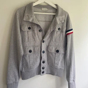 Grå Moncler Cardigan - Tja säljer denna skit feta cardigan/overshirt ifrån Moncler, 10/10 skick, Det är en gammal Moncler modell och är storleken S men passar därmed en Xs, passar er mellan 165-169 bäst, perfekt nu inför hösten, har du fler frågor kom privat. (Priset är ej fast) buda på!